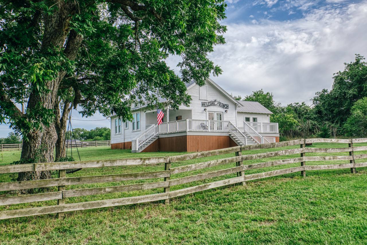 White farmhouse with wraparound porch, swing tree, and American flag