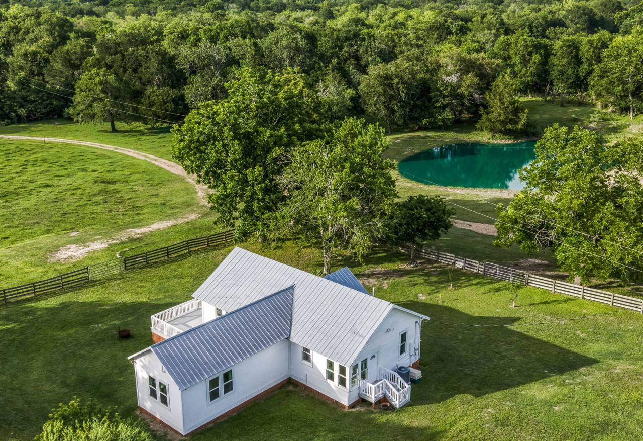 Aerial view of farmhouse with stocked pond and rolling acreage — 19576 Pickens Rd Washington TX